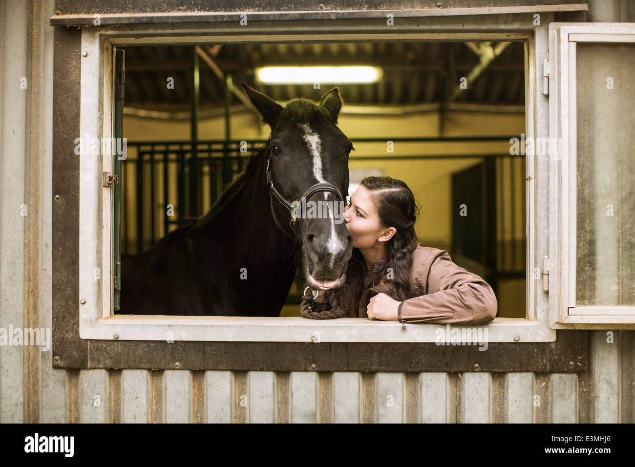 Junge Frau küssen Pferd im Stall Stockfoto