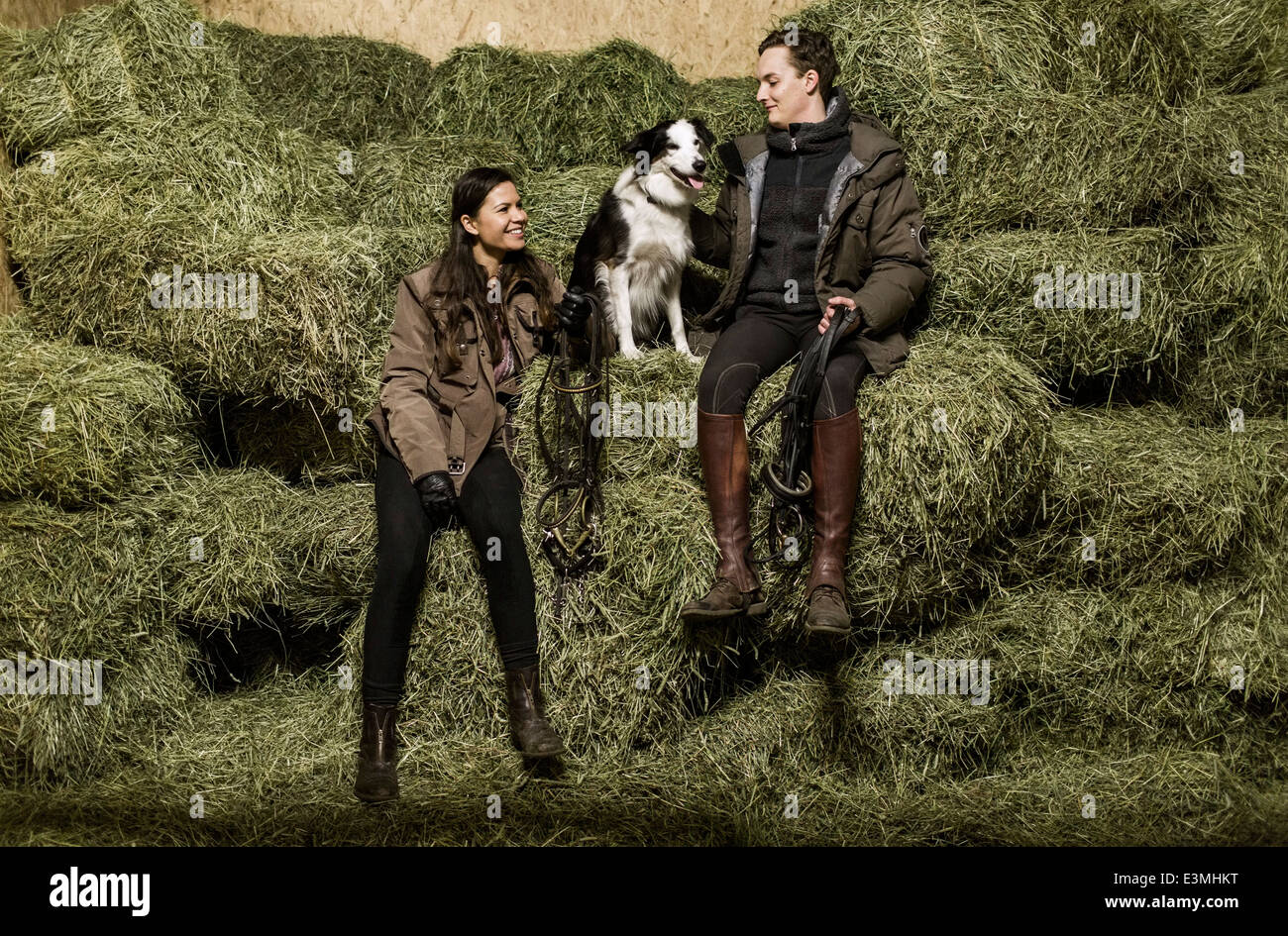 Voller Länge Rückansicht des jungen Brautpaar mit Hundesitting auf Heuhaufen im Stall Stockfoto