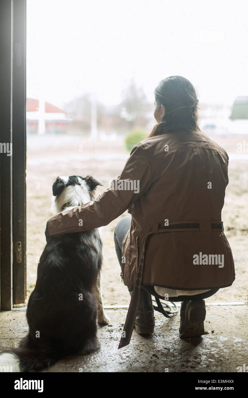 Voller Länge Rückansicht der jungen Frau Arm um Hund in Tür Pferdestall Stockfoto