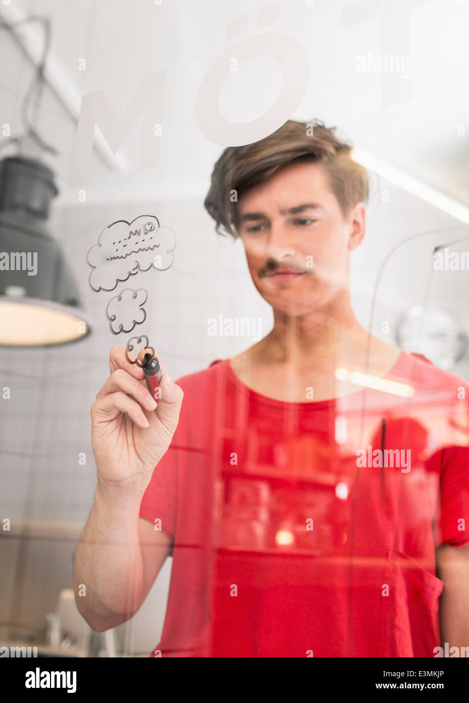 Junger Geschäftsmann ziehen Wolken auf transparentem Glas in Kreativbüro Stockfoto