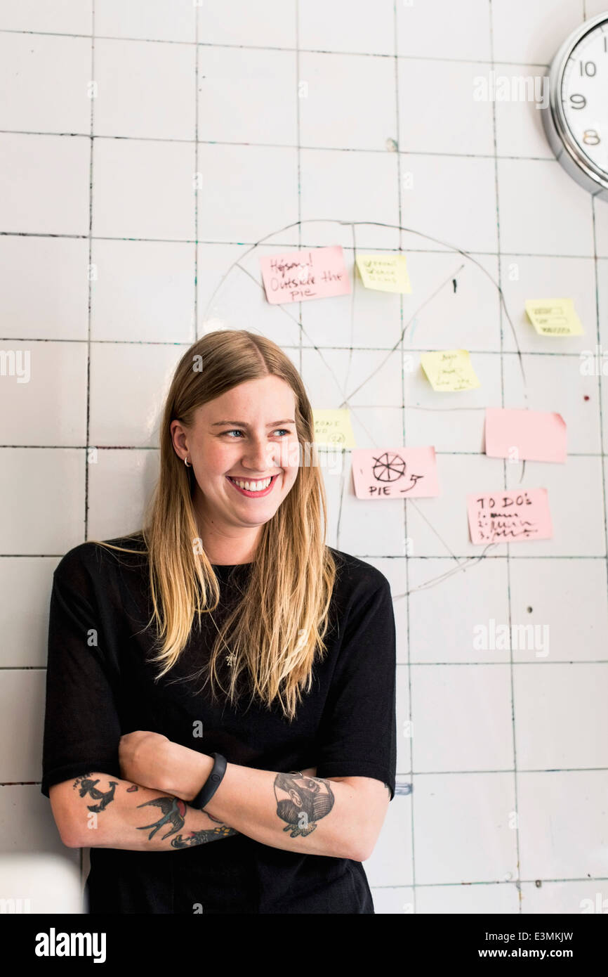 Lächelnde junge Geschäftsfrau steht vorne an Wand mit Haftnotizen im neuen Büro Stockfoto