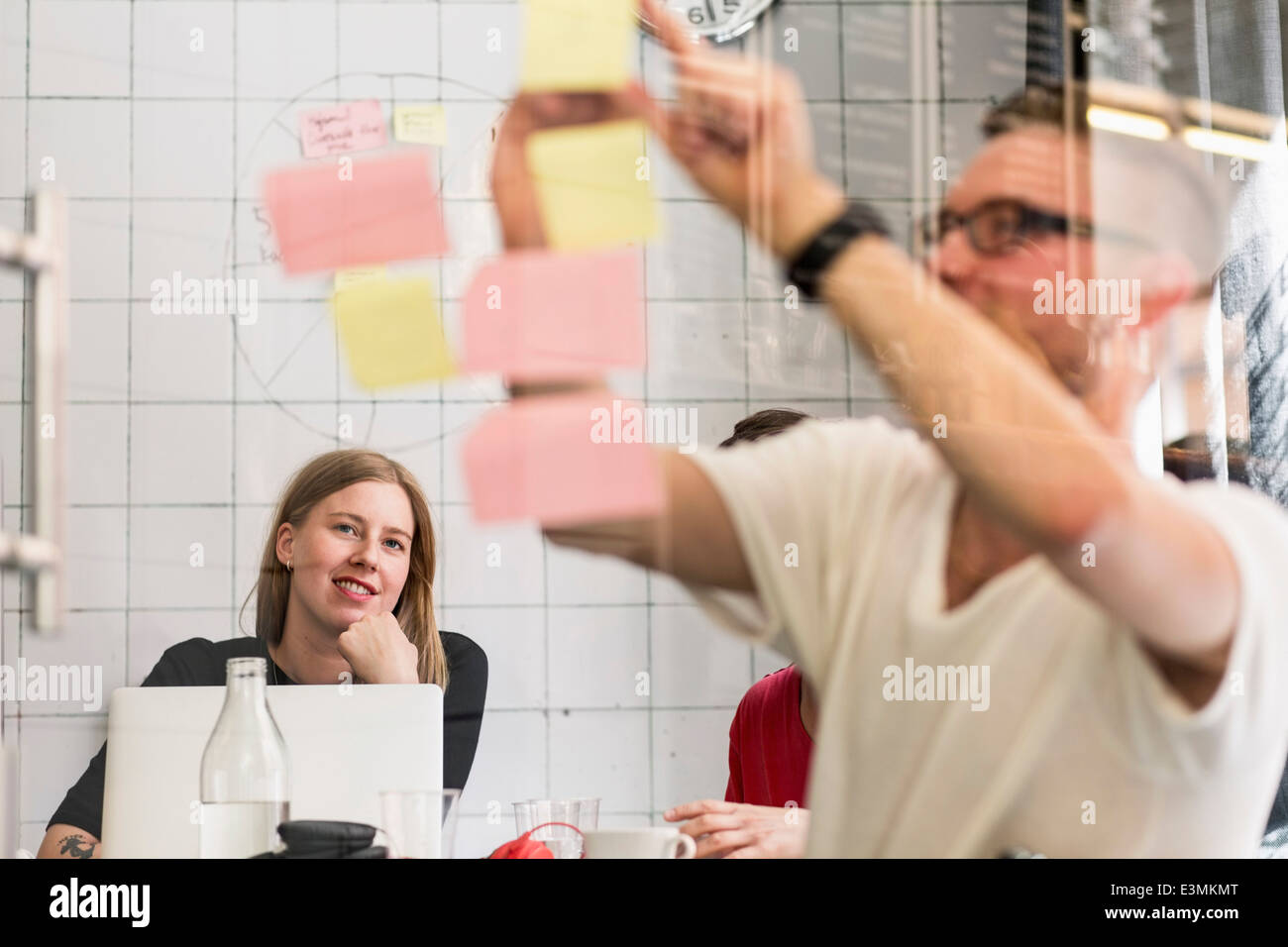 Junger Geschäftsmann schreiben Ideen auf selbstklebende Noten mit Kollegen im Hintergrund bei Kreativbüro Stockfoto
