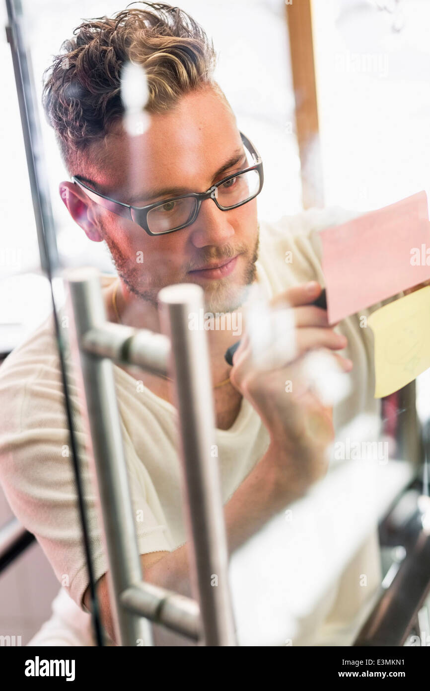 Junger Geschäftsmann Klebstoff Notizenschreiben auf transparentem Glas im neuen Büro Stockfoto