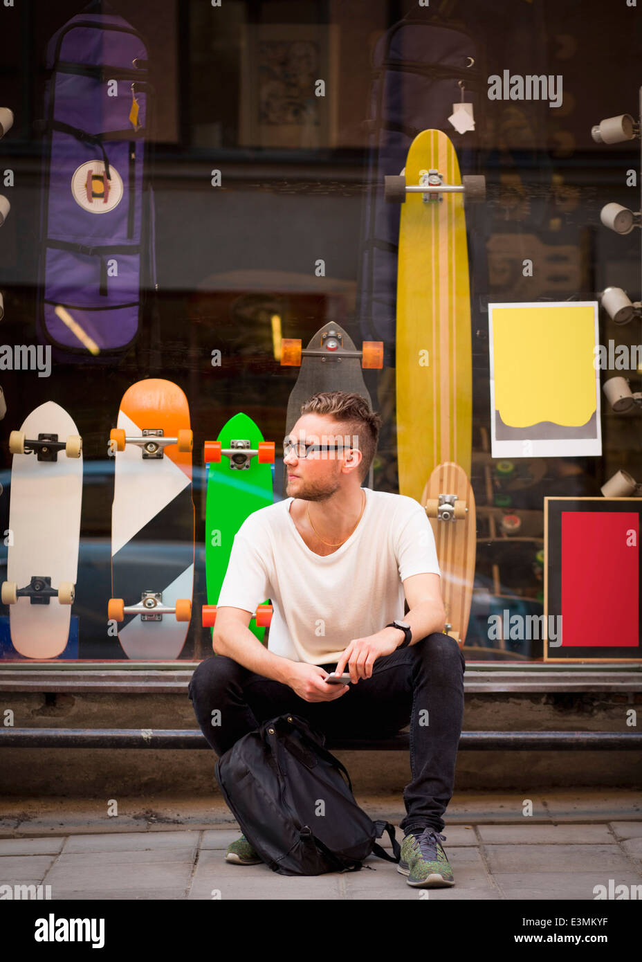 Gesamte Länge der junge Mann sitzt außen Skateboard shop Stockfoto