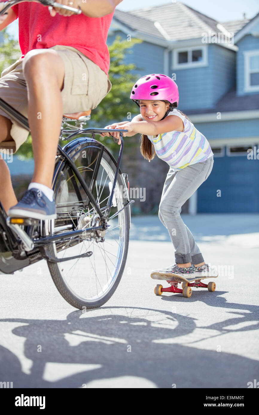 Tochter auf Skateboard Vater auf dem Fahrrad schieben Stockfoto