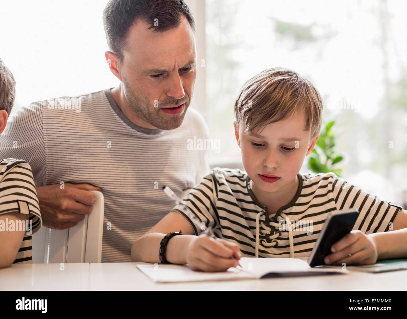 Junge mit Handy während des Schreibens am Tisch von Vater im Haus Stockfoto