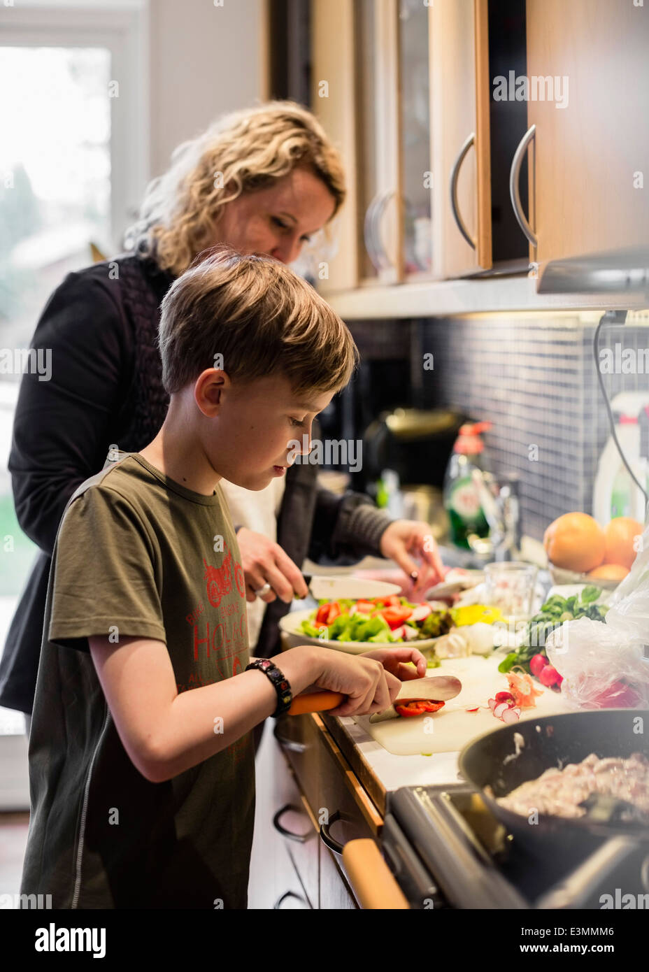 Sohn und Mutter Schneiden von Gemüse in der Küche Stockfoto