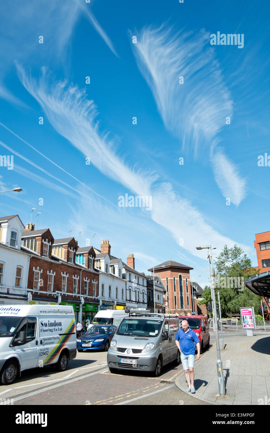 Feder wie Cirrus Wolkenformationen in einem azurblauen Sommerhimmel über eine typisch britische Straßenszene Stockfoto