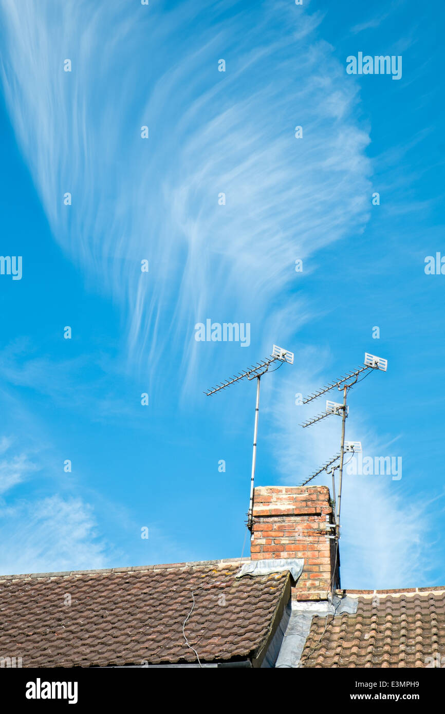 Eine Feder wie Cirrus Wolkenbildung über eine auf dem Dach & Schornstein mit Antennen gegen einen azurblauen Sommerhimmel Stockfoto