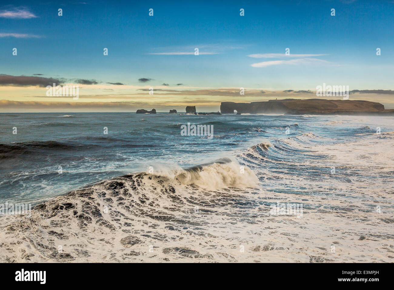 Wellen am Ufer mit Dryholaey im Hintergrund, Island. Dyrhólaey übersetzt bedeutet "die Tür Loch-Insel" Stockfoto