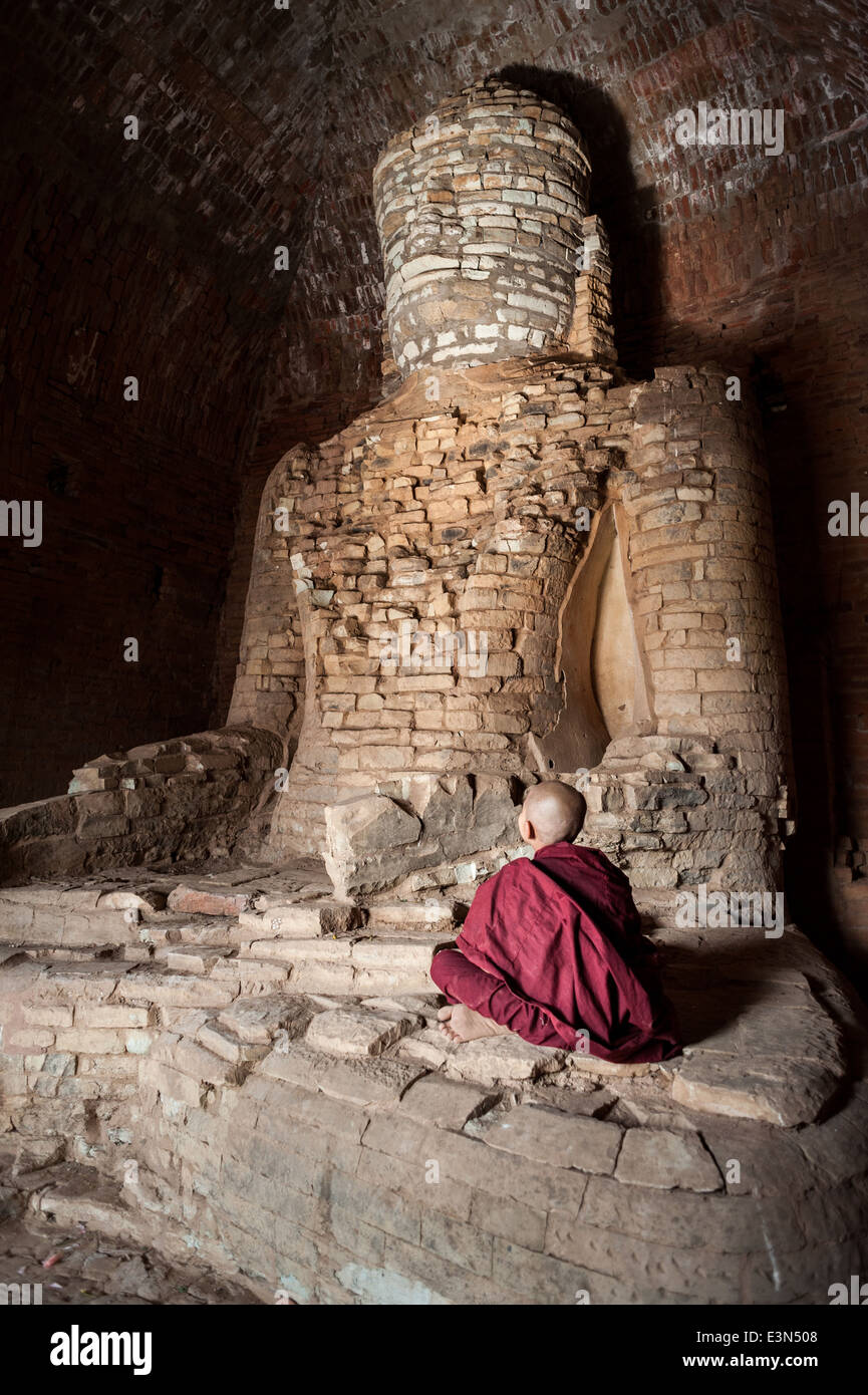 Junger Mönch sitzt vor einem alten Statue von Buddha, Bagan, Myanmar, Asien. Stockfoto