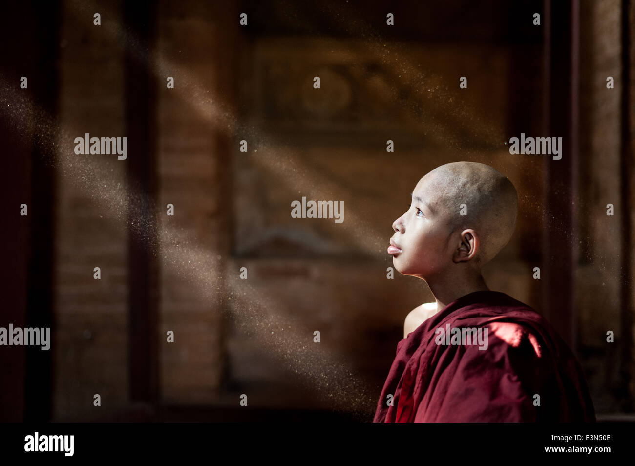 Junger Mönch schaut aus dem Fenster. Strahlen der Sonne zeigt den Staub in der Luft, Bagan, Myanmar, Asien Stockfoto
