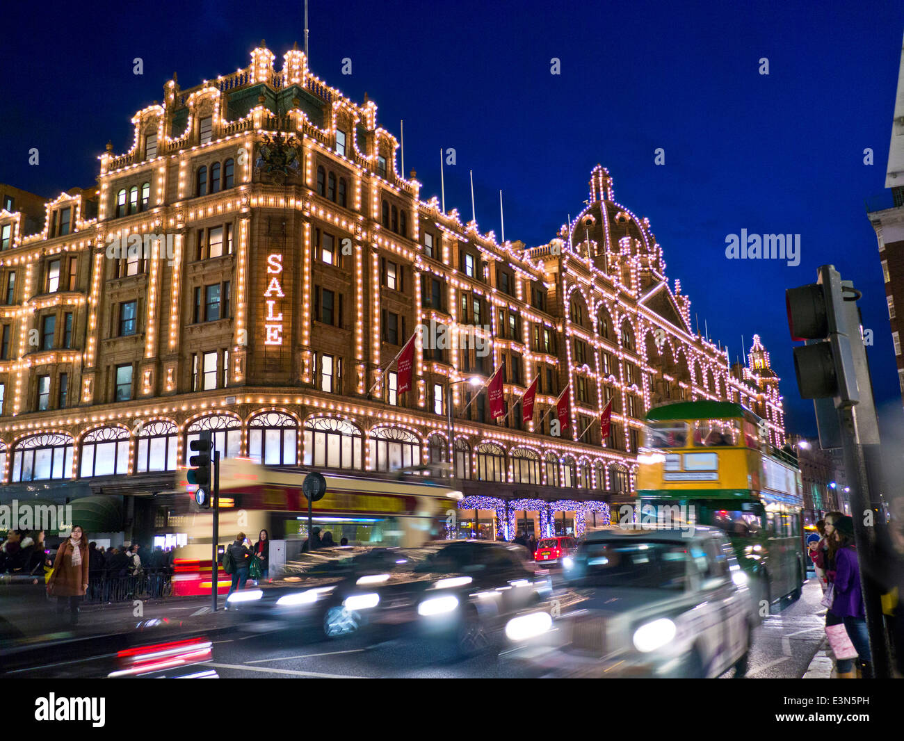 Das Kaufhaus Harrods in der Abenddämmerung mit beleuchteten "Sale" Schild Shopper Vintage-Tourbus und vorbeifahrenden Taxis Knightsbridge London SW1 Stockfoto