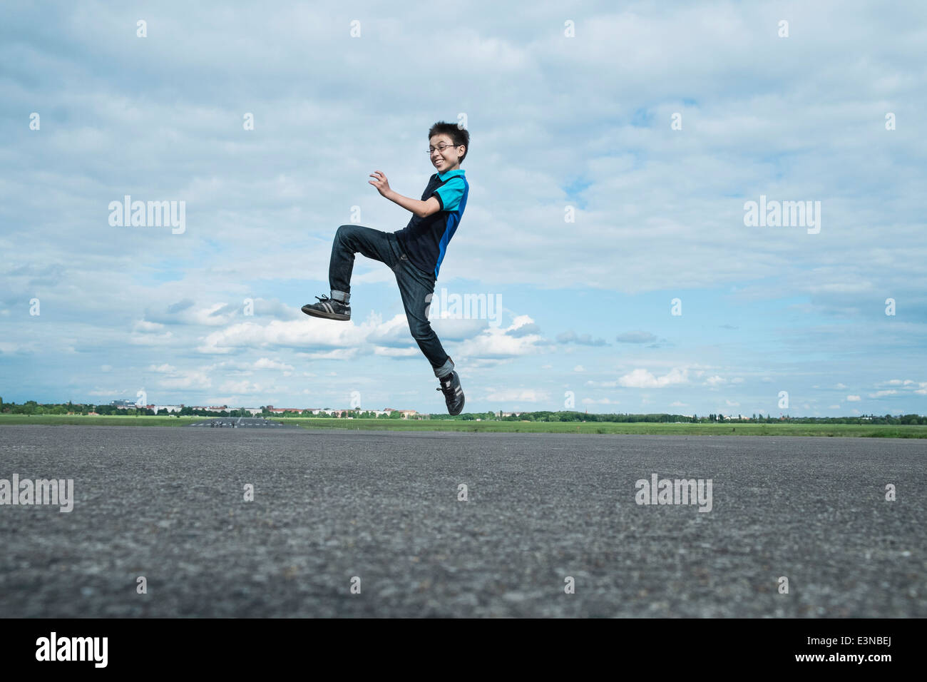 Voller Länge begeistert junge auf der Straße gegen bewölktem Himmel springen Stockfoto