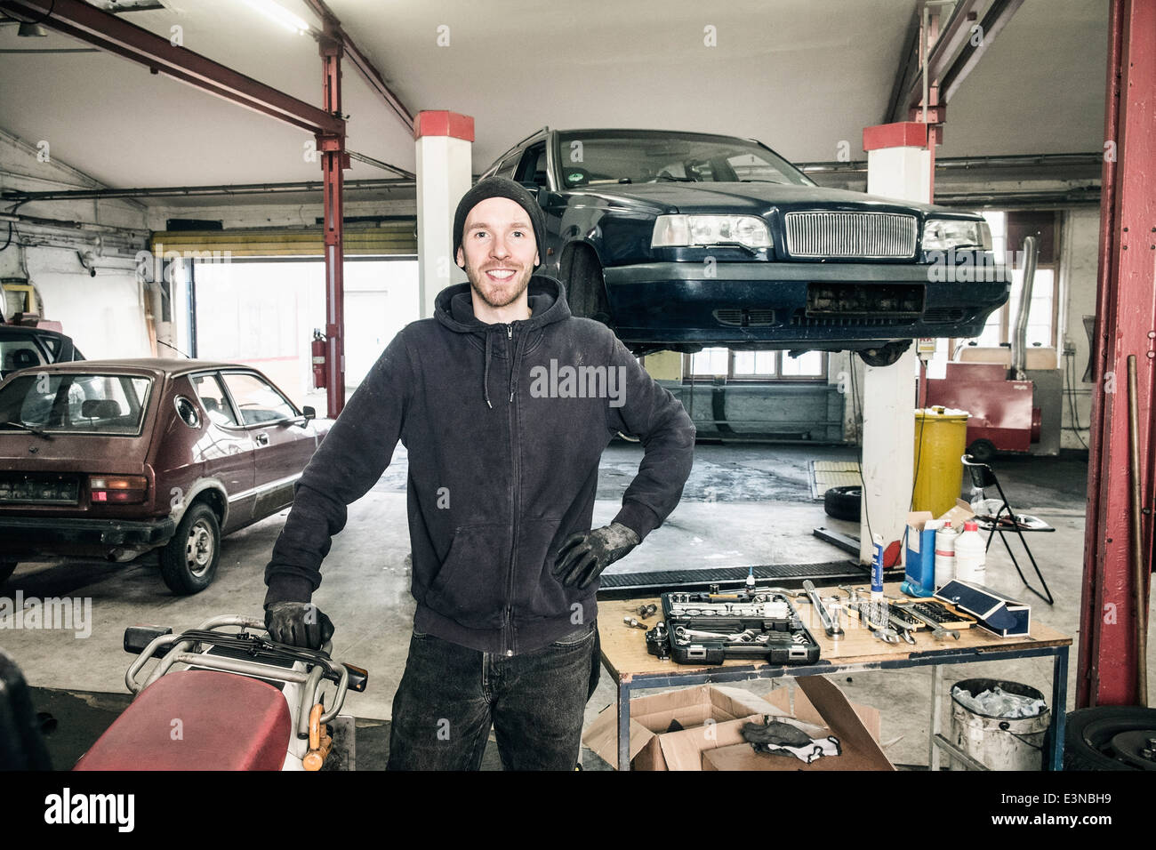 Porträt von zuversichtlich männlichen Auto Mechaniker stehend mit der Hand auf die Hüfte in Werkstatt Stockfoto