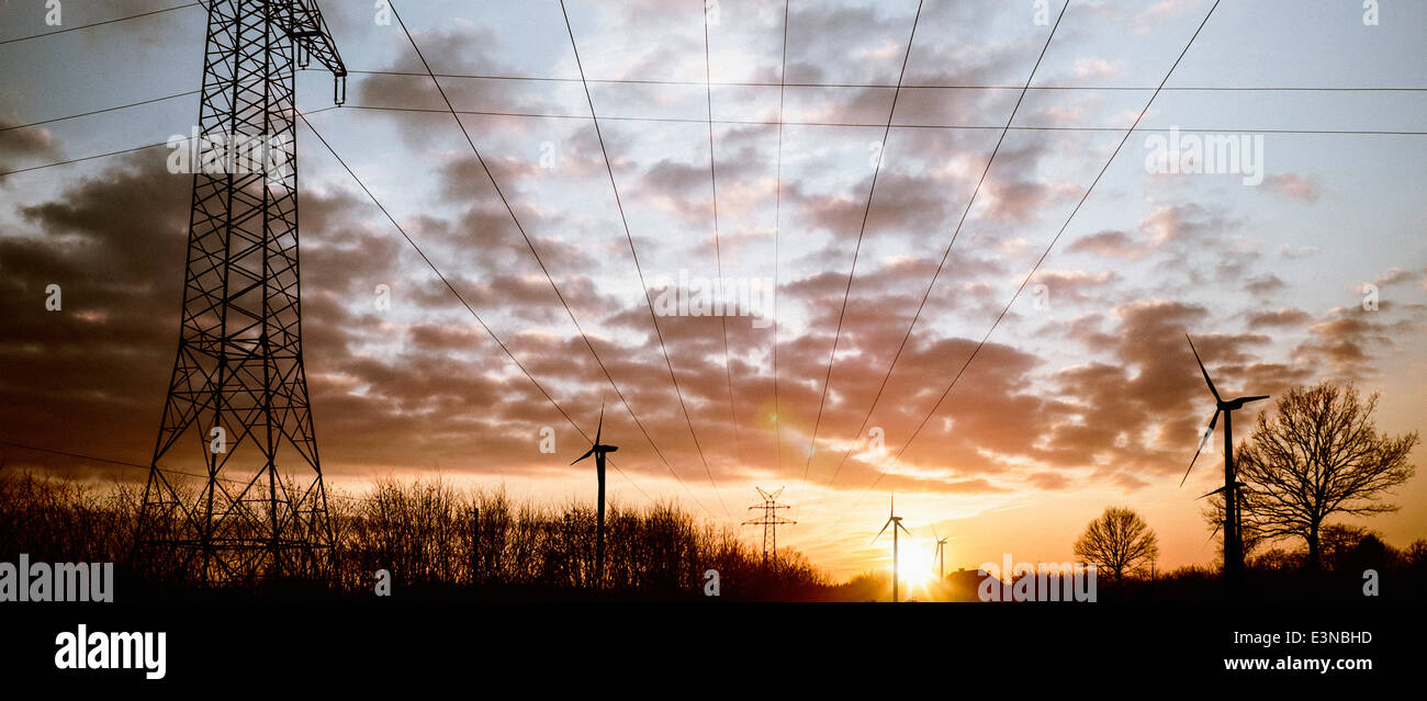 Strommasten und Windräder gegen bewölktem Himmel in der Abenddämmerung Stockfoto