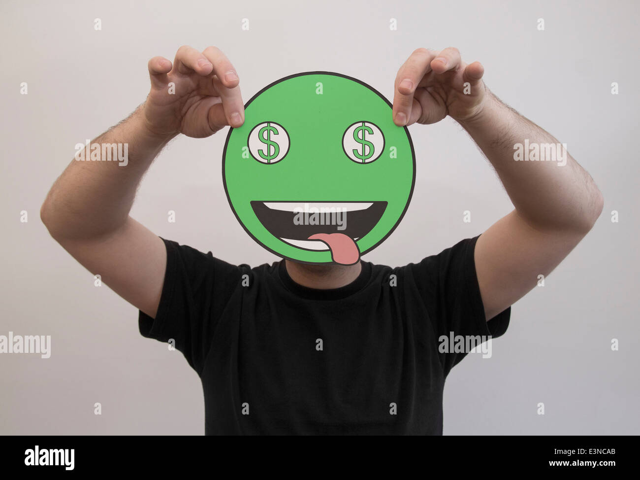 Mann, der ein grünes Dollarzeichen Emoticon Gesicht vor sein Gesicht hält Stockfoto