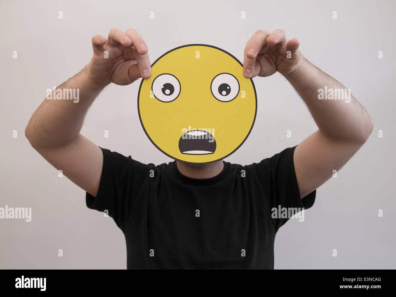 Mann, der ein Gesicht schockiert Emoticon vor sein Gesicht hält Stockfoto