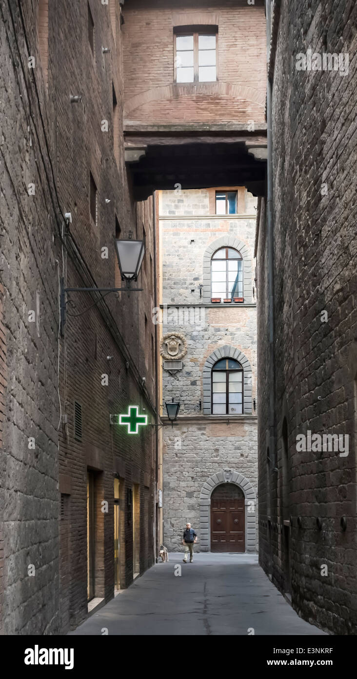 Mensch und Hund in dunklen Gasse finden Sie das gemütliche Licht einer Apotheke im Trübsinn: Siena, Toskana, Italien Stockfoto