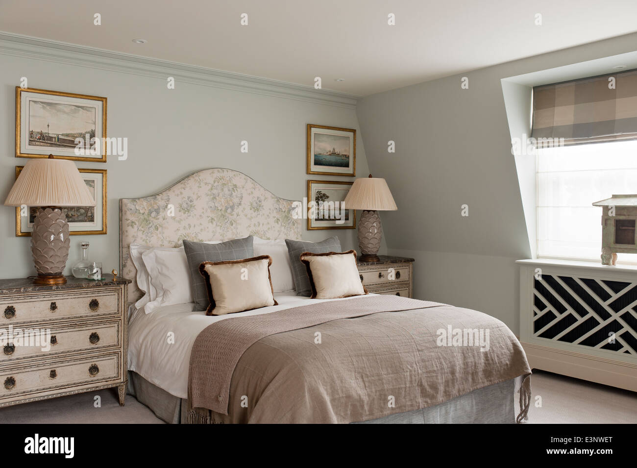 Elegantes Schlafzimmer in Erdtönen mit floral gemusterten Bett, flankiert von zwei Holzkisten mit Lampen Stockfoto