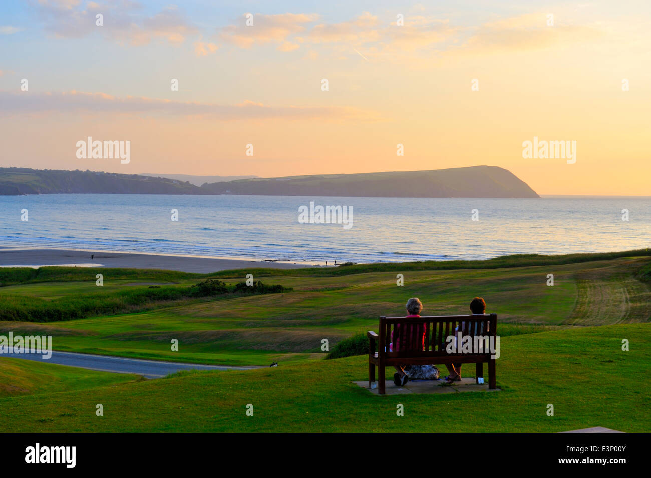Newport Links Golf Club Sonnenuntergang, Frau auf der Bank mit Blick auf Dinas Kopf Halbinsel, Newport, Pembrokeshire, Wales, UK Stockfoto