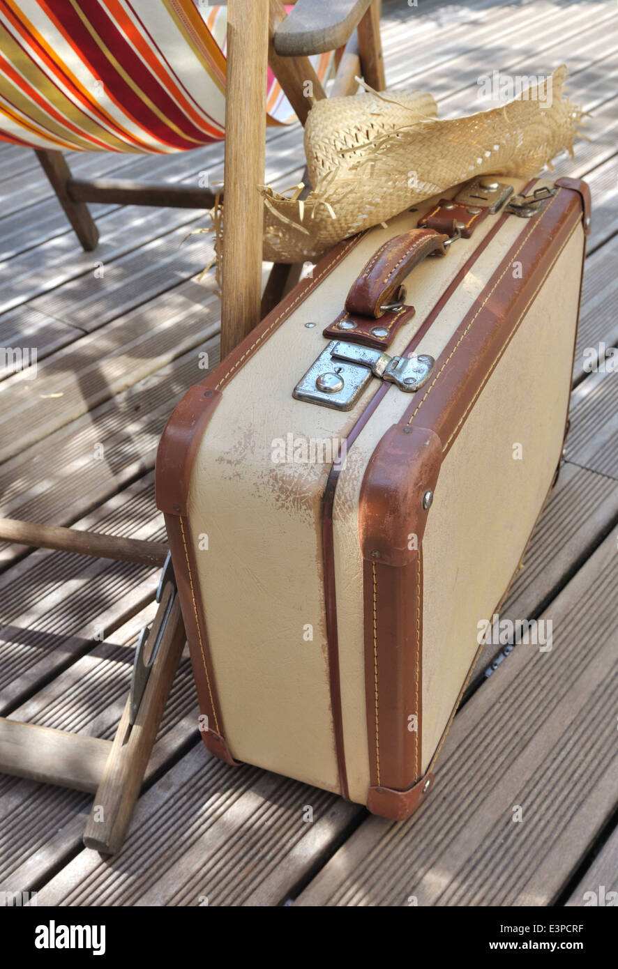 Strohhut auf kleine Retro-Koffer neben einem Liegestuhl auf Holzterrasse Stockfoto