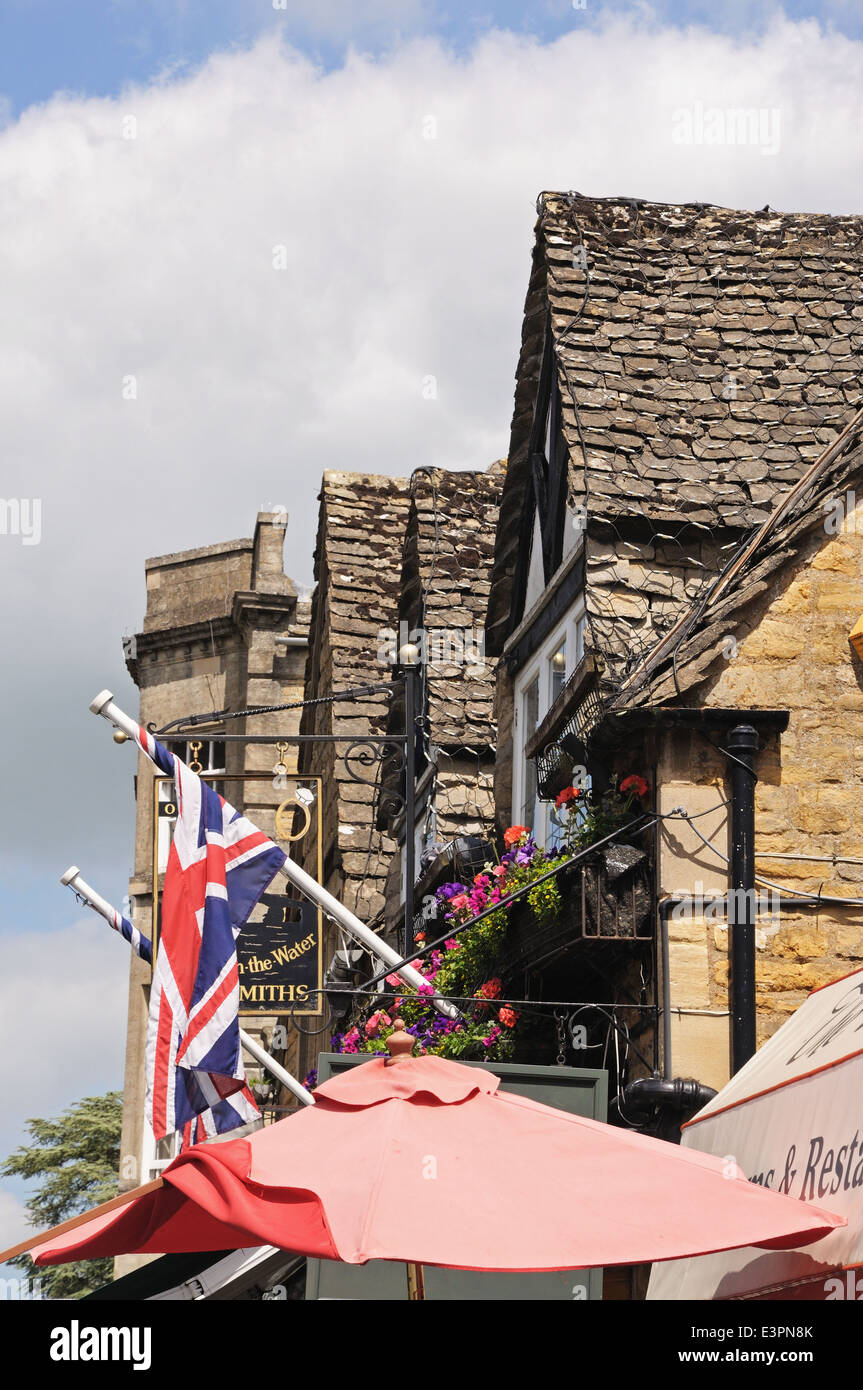 Blick auf die Spitzen der Dorf-Gebäude mit Flaggen und Sonnenschirmen unten, Bourton am Wasser, England, UK. Stockfoto