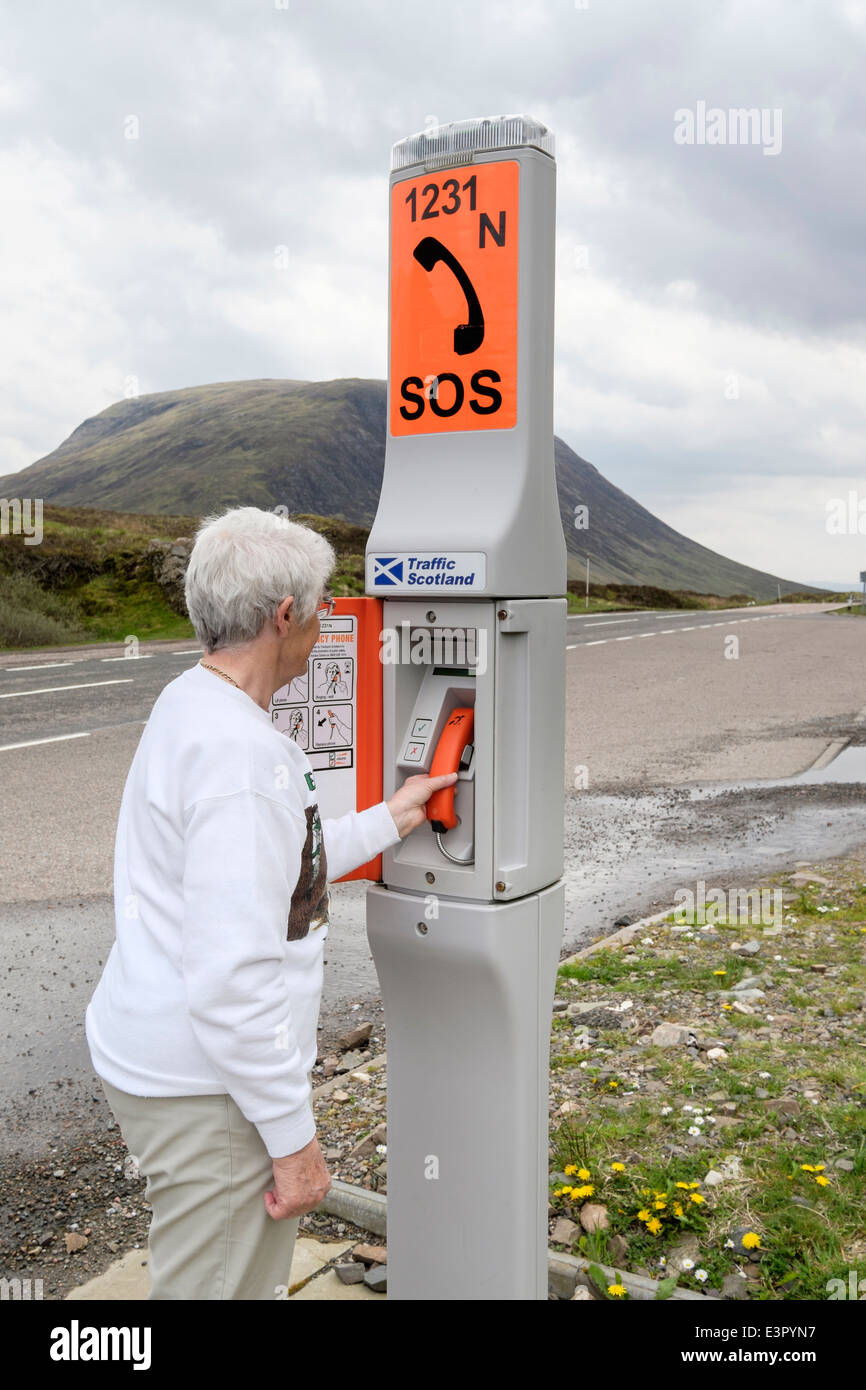 Ältere Frau mit einer SOS-Notruf neben einer abgelegenen Landstraße. Glen Coe, Highland, Schottland, Großbritannien Stockfoto