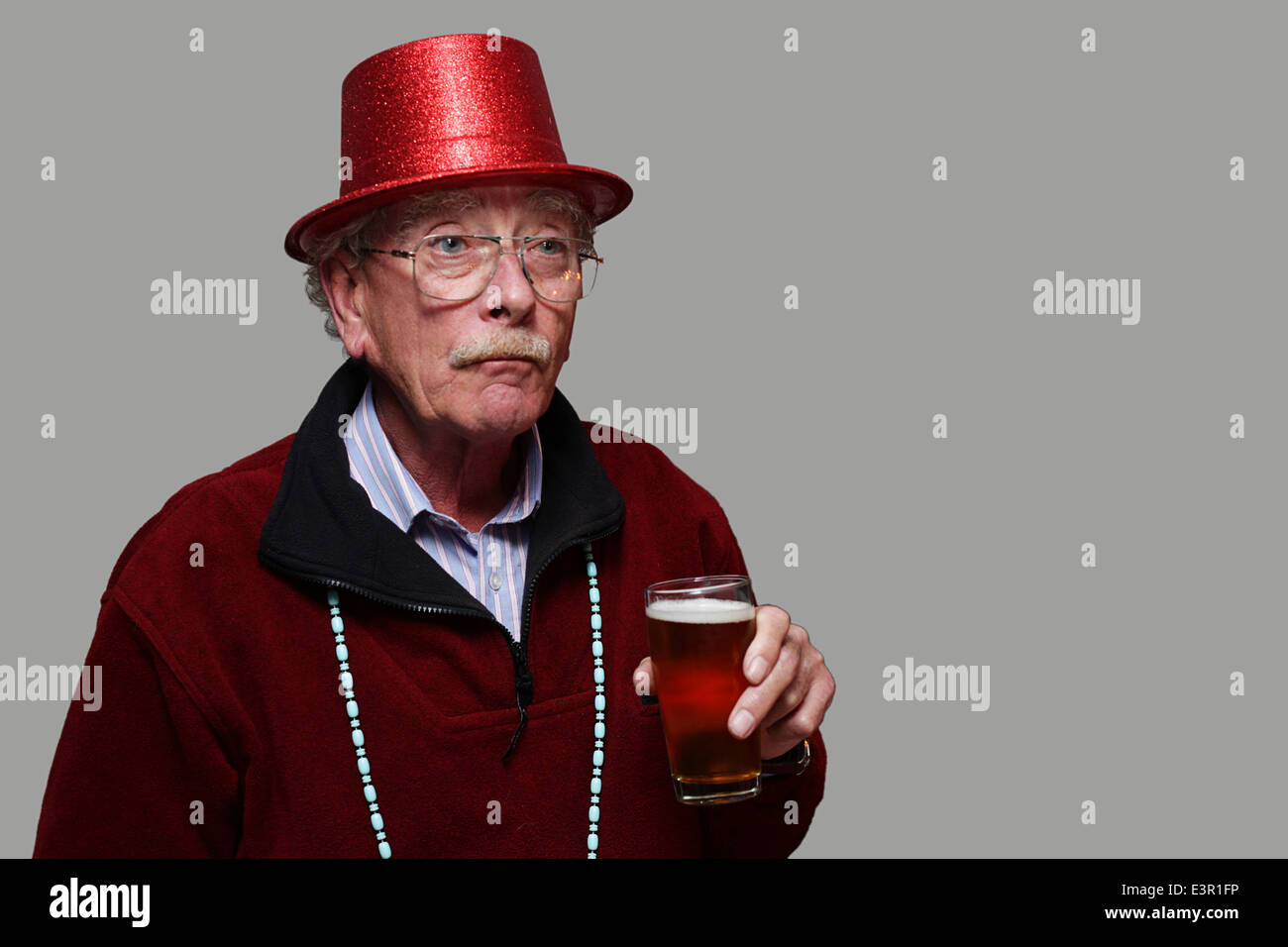 Ein älterer Mann in einem roten Partyhut mit einem Glas Bier Stockfoto