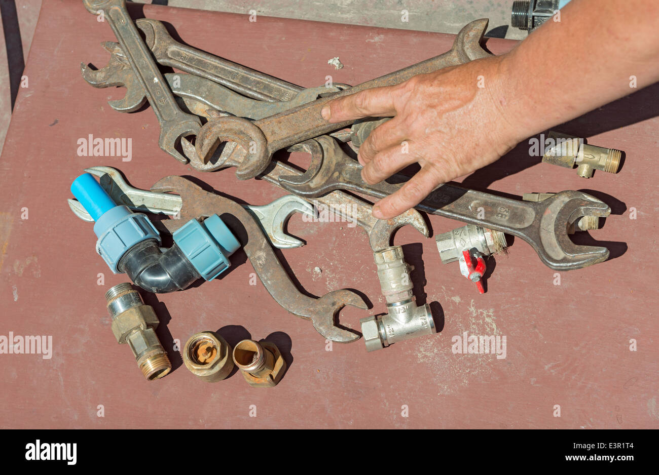Viele rostige Schlüssel und Ventile mit streckte die Hand aus der Hand des Klempners auf braunem Hintergrund. Stockfoto