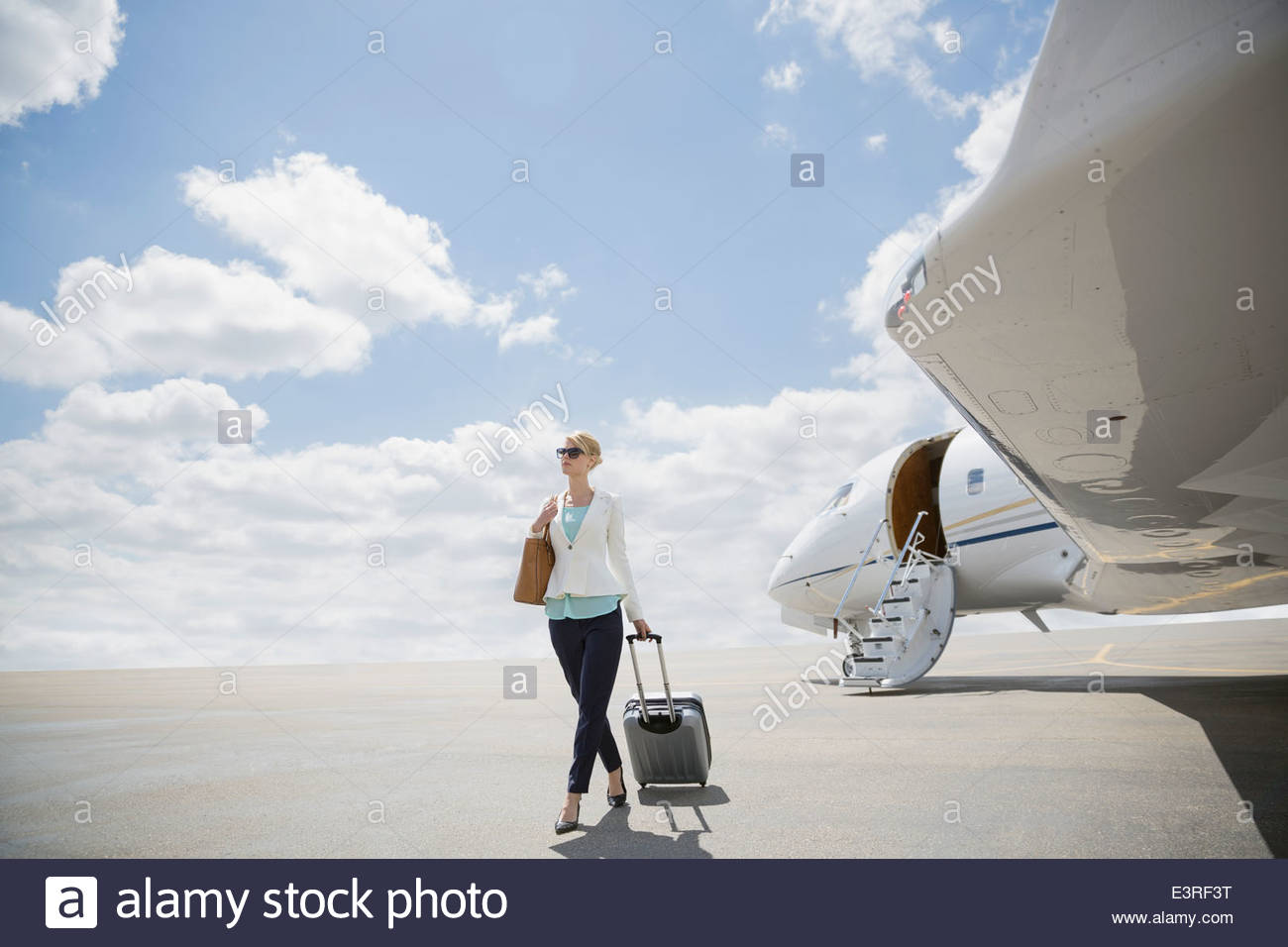 Geschäftsfrau ziehen Koffer auf Asphalt in der Nähe von Geschäftsreiseflugzeugen Stockfoto