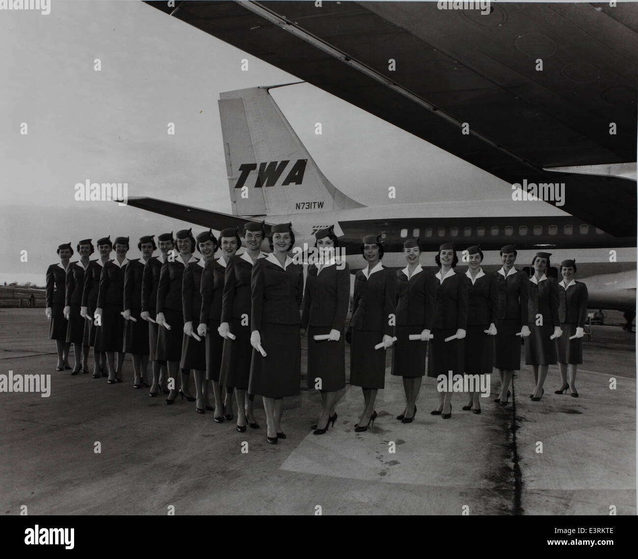 Dieses Bild zeigt eine Stewardess vor einer Boeing 707-131C, einem wichtigen Flugzeug in der frühen kommerziellen Luftfahrt. Die Boeing 707 war ein Pionierflugzeug, das von Fluggesellschaften wie Trans World Airlines (TWA) und Lukim Air Service eingesetzt wurde. Das Foto zeigt auch die Rolle der Frauen in der Luftfahrt als Stewardessen Mitte des 20. Jahrhunderts. Stockfoto