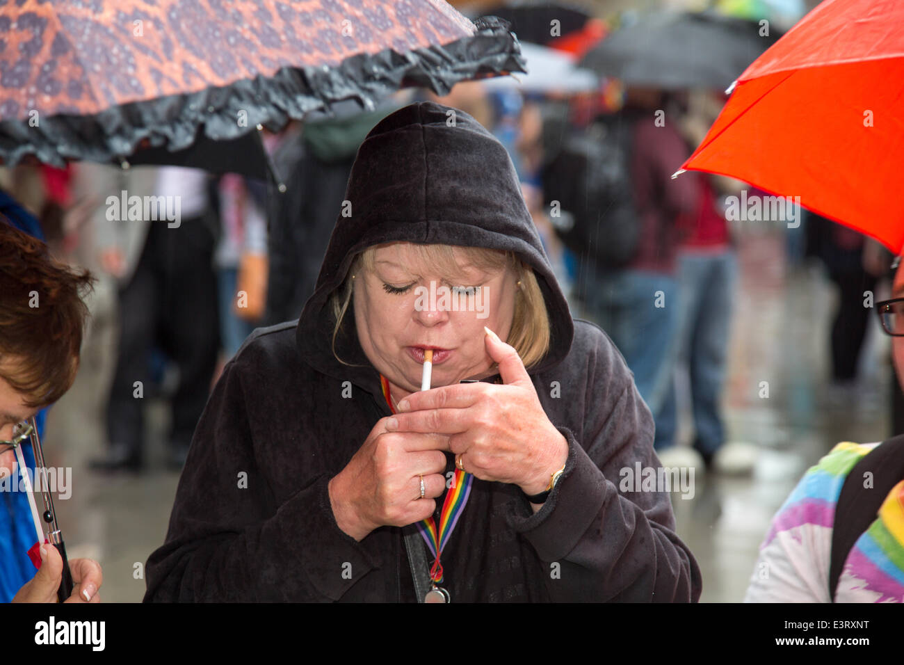 Eine Frau zündet sich eine Zigarette während einer sehr nassen und feuchten Gay Pride. Stolz zog Tausende Besucher trotz der kräftigen Schauern. Stockfoto