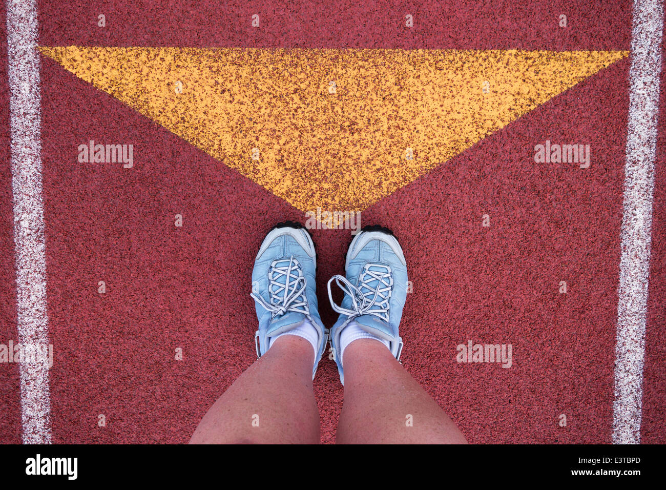 Ein Läufer steht mit ihren Schuhen zeigte auf ein gelbes Dreieck auf einer roten Laufstrecke. Stockfoto