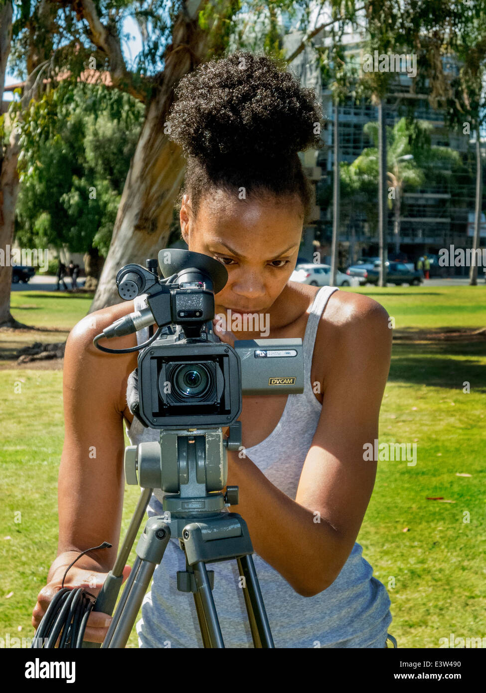 Eine junge afrikanische amerikanische Studentin Kommunikation bereitet sich auf eine Interview mit einer Videokamera aufnehmen im Balboa Park, San Diego, Kalifornien. Stockfoto