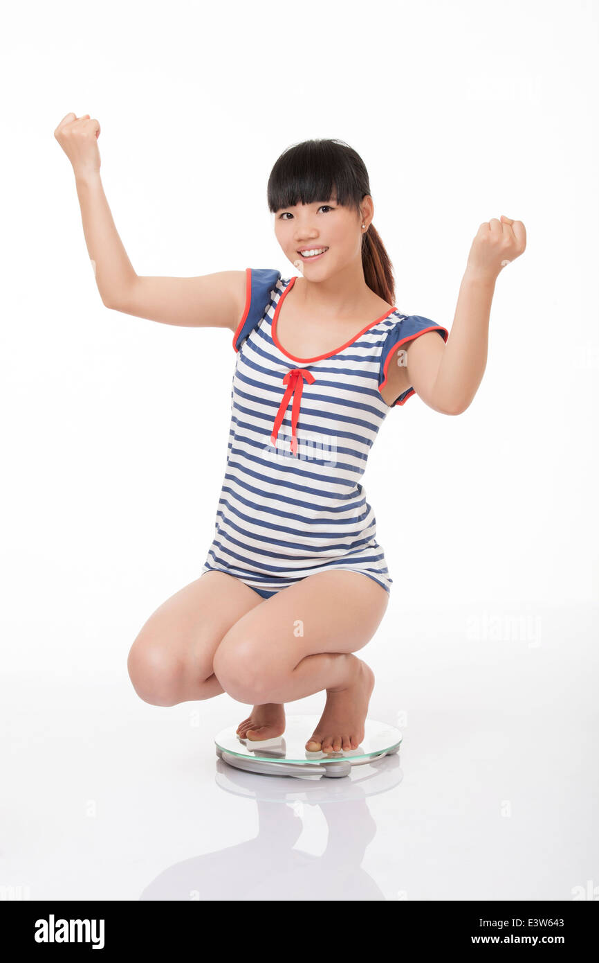 Schöne chinesische Frau wiegen sich auf einer Skala und begeistert mit den Ergebnissen, die auf einem weißen Hintergrund isoliert Stockfoto