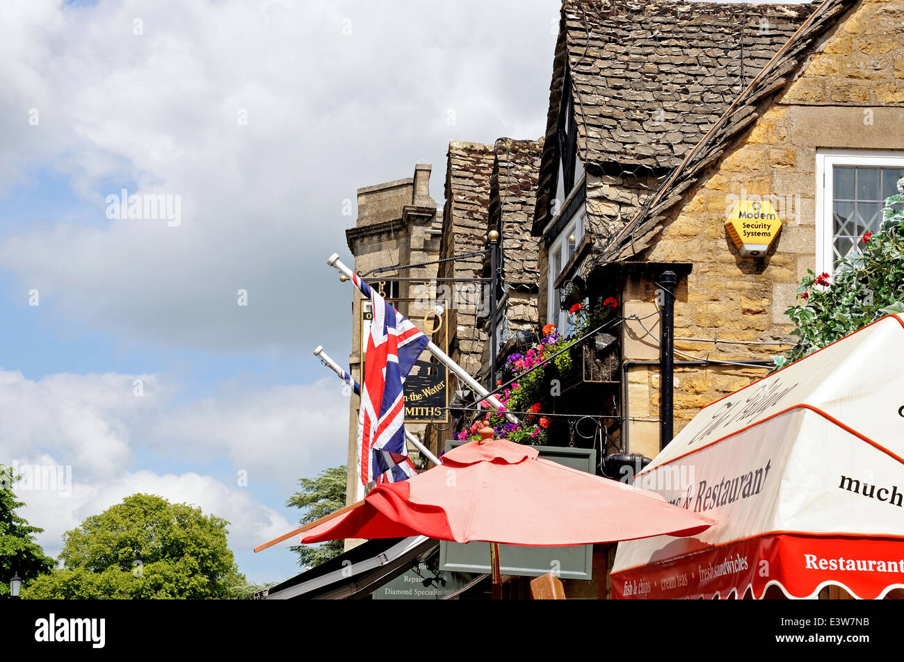 Blick auf die Spitzen der Dorf-Gebäude mit Flaggen und Sonnenschirmen unten, Bourton am Wasser, England, UK, Westeuropa. Stockfoto
