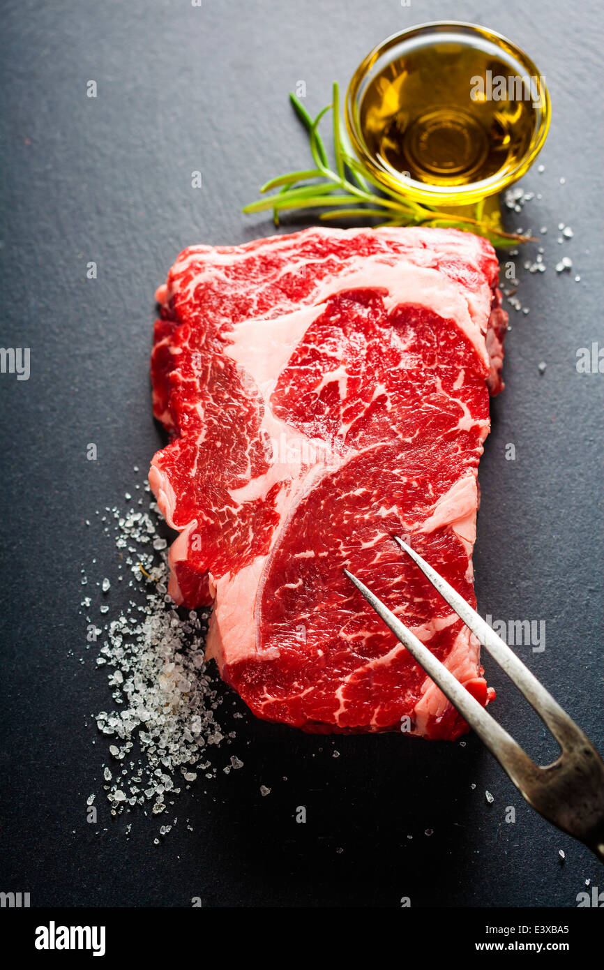 Rohes Rindfleischsteak mit Fleischgabel auf dunklem Schiefer Hintergrund Stockfoto