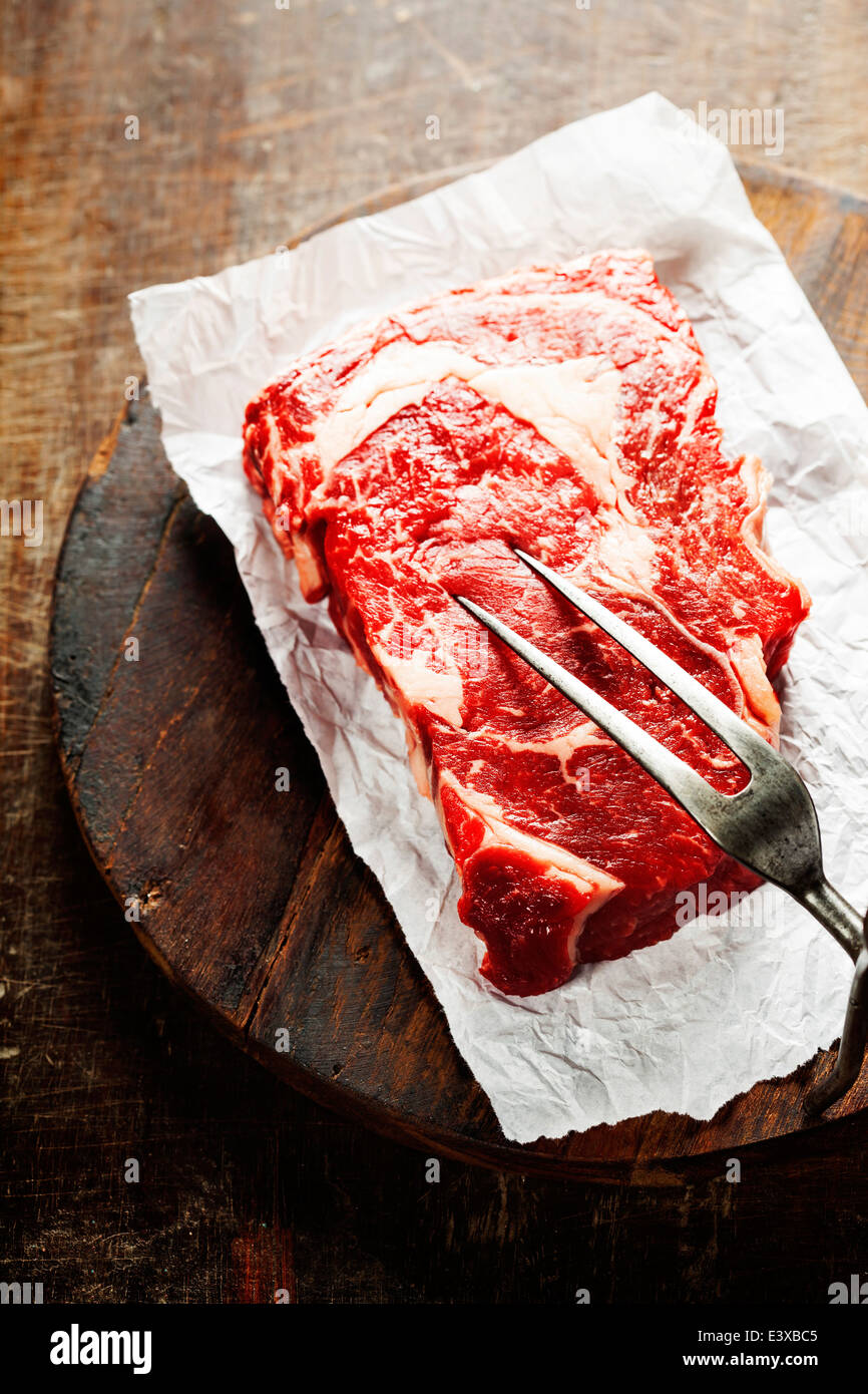 Rohes Rindfleischsteak mit Fleischgabel auf einem alten Holztisch Stockfoto