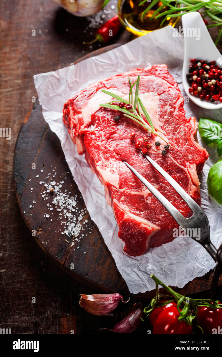 Rohes Rindersteak mit Fleischgabel und Zutaten auf hölzernen Hintergrund Stockfoto