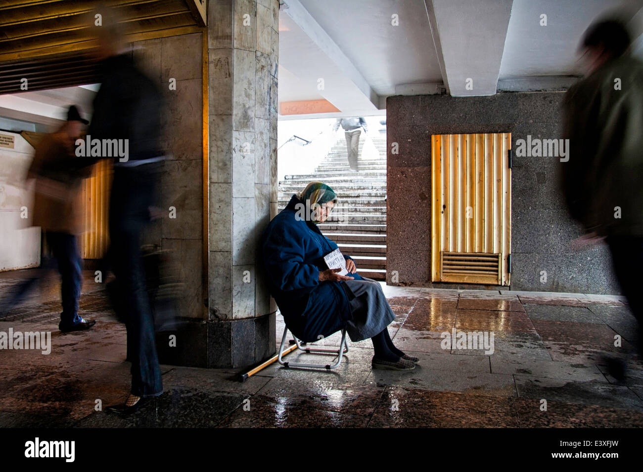 Ein Bettler Frau sitzt an einem regnerischen Tag in einen unterirdischen Gang Stockfoto