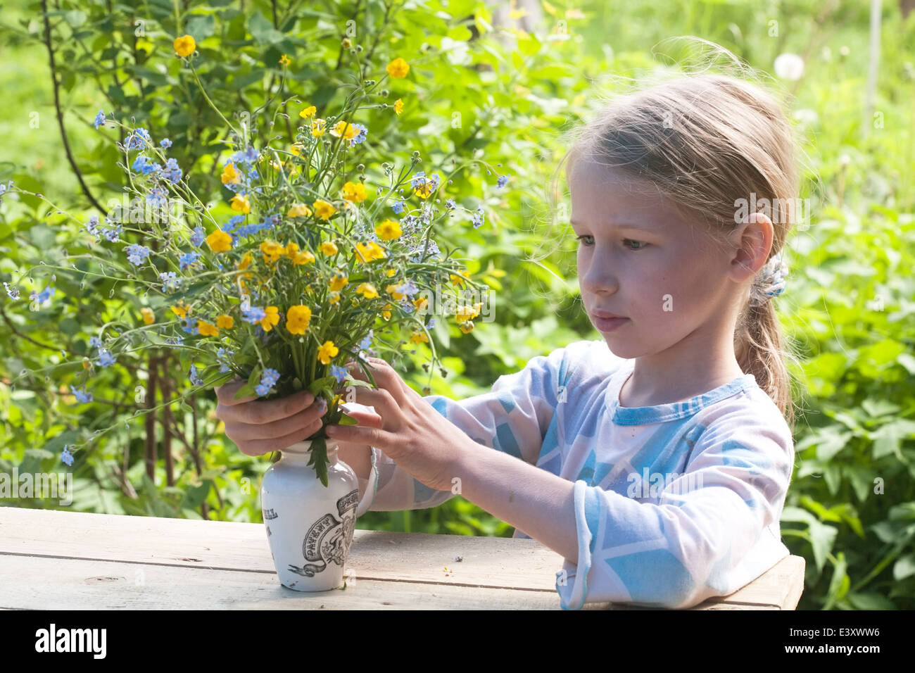 kleines Mädchen Umsetzung Blumenstrauß Sommer Wild um die alte Vase auf Holztisch Stockfoto