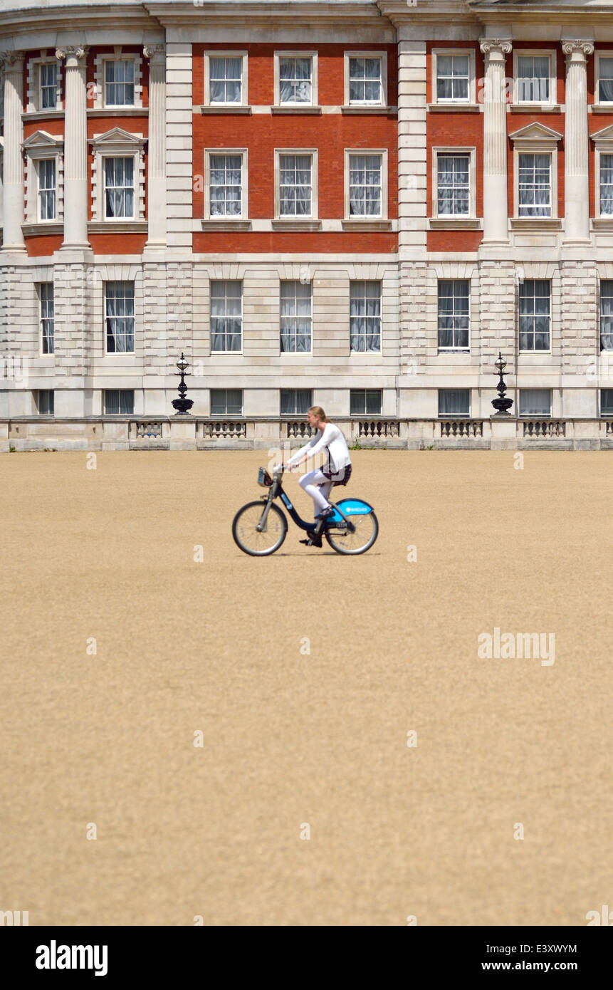 London, England, Vereinigtes Königreich. Frau reitet ein 'Boris Bike' in Horse Guards Parade. (Gebäude im Fokus - Radfahrer leicht verschwommen) Stockfoto