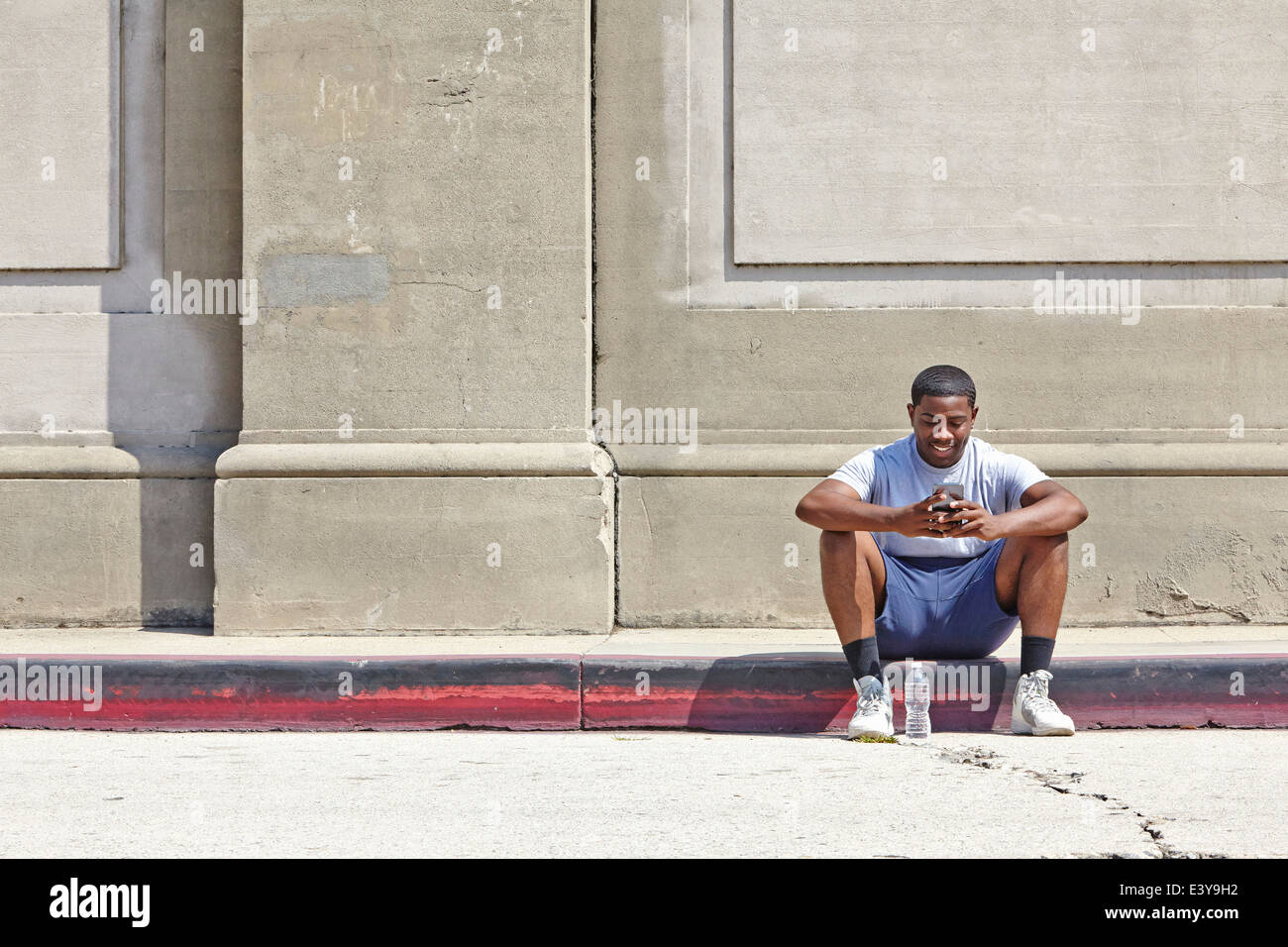 Junge männliche Läufer sitzen auf Bürgersteig SMS auf smartphone Stockfoto