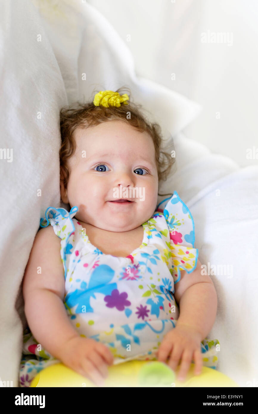 Ein drei Monate altes kaukasische Baby Girl, lächelnd und mit Blick auf die Kamera. Oben sitzen. Hintergrund teilweise mit Weiß gefüllt. Stockfoto