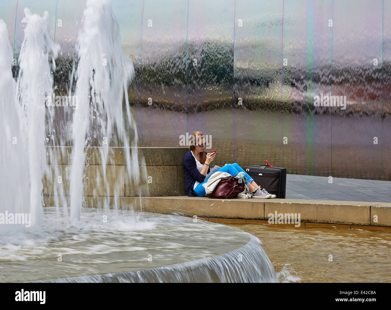 Junge Frau entspannende und sms durch die Wasserspiele von Bahnhof Sheffield. Freier Platz für Text Stockfoto