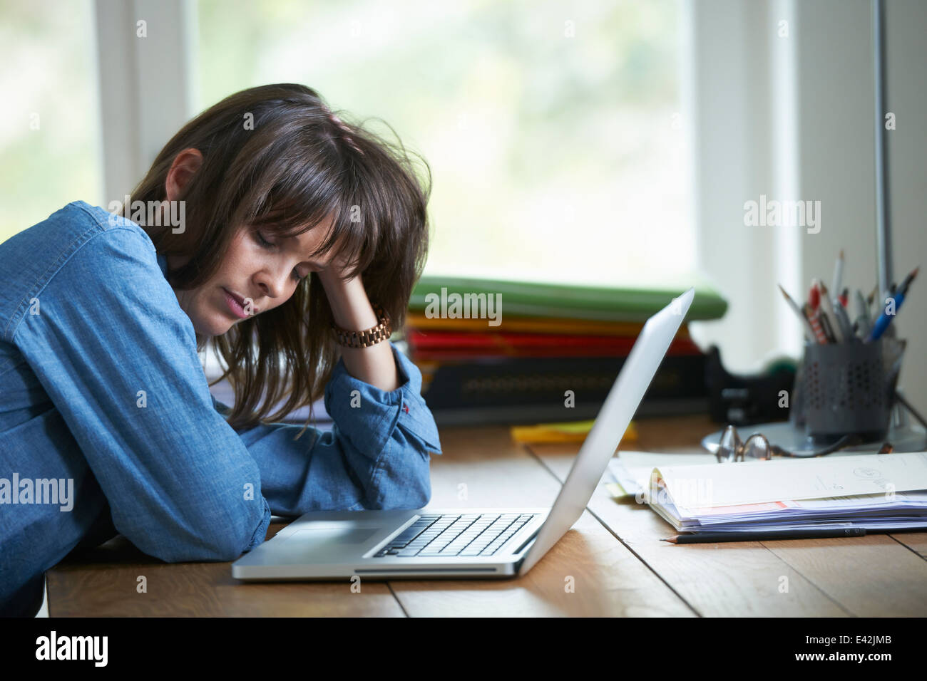 Frau sitzt am Schreibtisch mit Laptop, Augen geschlossen Stockfoto