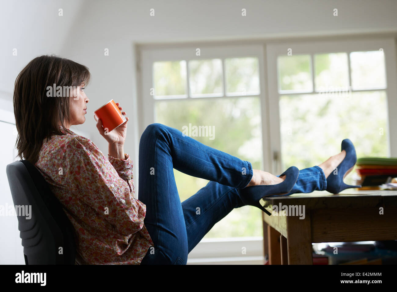 Reife Frau mit Füßen auf Schreibtisch, Kaffee trinken Stockfoto