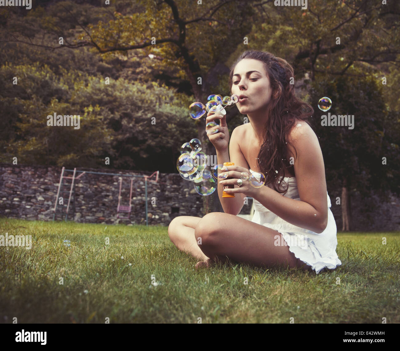 Junge Frau sitzt im Feld Seifenblasen Stockfoto