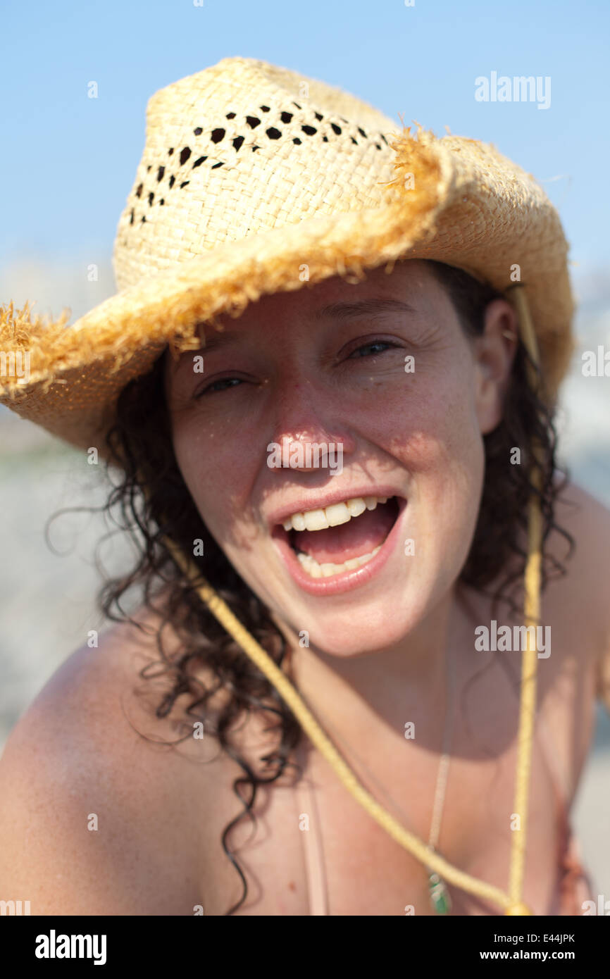 Lächelnde Frau mit lockigem Haar und Cowboy-Hut am Strand im Sommer. Stockfoto